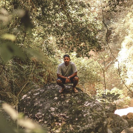 O petropolitano Matheus Lima Teko agachado em uma pedra em meio a natureza. Fotografia de Tiago Fernandes.